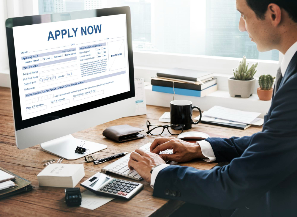 Professional completing an online application form on a desktop computer with ‘Apply Now’ displayed on screen.